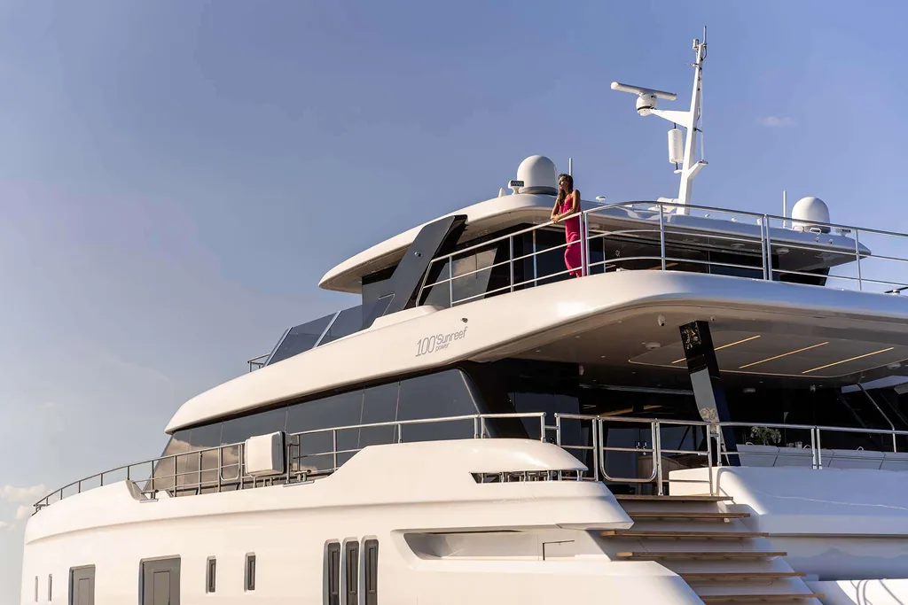 Osoba stojąca na pokładzie luksusowego jachtu Sunreef Yachts z jasnym niebem w tle.