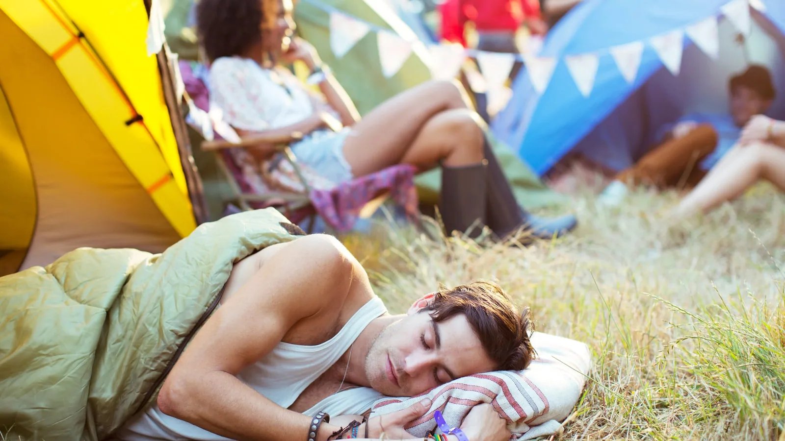 Man sleeping on grass outside of a tent at a music festival.