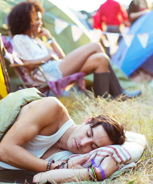 Man sleeping on grass outside of a tent at a music festival.