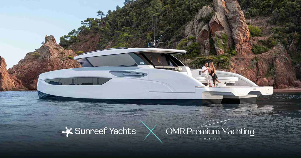 A luxurious white yacht by Sunreef Yachts is docked near rocky cliffs with green vegetation. Two people are seated on the deck enjoying the scenic view. The log