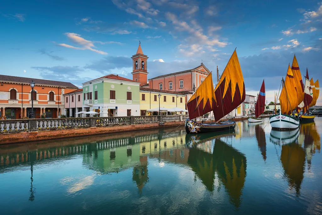 Cesenatico canal, historic wooden sailboats and church at sunset. Emilia Romagna region, Forlì Cesena province, Italy