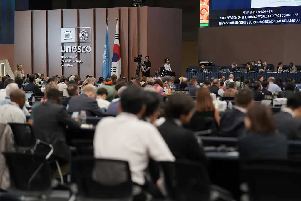 Sala konferencyjna, tłum ludzi przy stolikach, logotyp 48. sesji Komitetu Światowego Dziedzictwa UNESCO